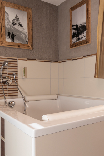 Ein modernes Badezimmer in unserem Luxusapartment für 6-8 Personen in Serfaus-Fiss-Ladis verfügt über eine weiße Badewanne mit beigen und braunen Fliesen. Über der Wanne zeigen zwei Schwarzweißfotos in Holzrahmen Bergszenen und ergänzen die strukturierten grauen und glatten Wände.