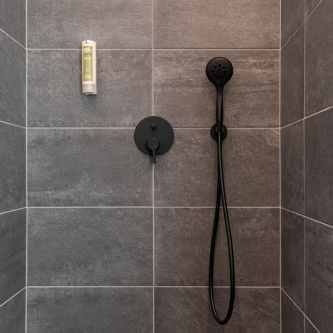 In einem Luxusapartment für 6-8 Personen in Serfaus-Fiss-Ladis besticht die moderne Dusche durch dunkelgraue Fliesen und einen eleganten, schwarzen, an der Wand montierten Duschkopf mit angeschlossenem Schlauch. Eine praktische Shampoo- oder Seifenflasche ist an der linken Wand angebracht und unterstreicht das minimalistische Design.