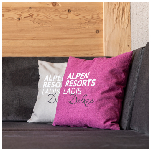 Zwei Kissen zieren das dunkle Sofa; eines ist rosa mit dem weißen Schriftzug „Alpen Resorts Ladis Deluxe“ und das andere ist hellgrau mit einem ähnlichen Text. Dahinter sorgt eine hölzerne Wandverkleidung für Wärme und weckt Erinnerungen an 3 Genussskitage inkl. 2. Tage Skipass.