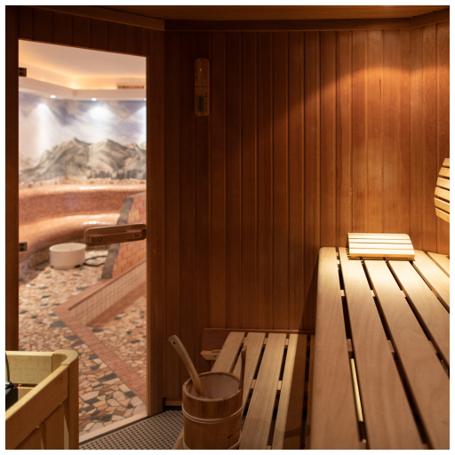 Gezeigt wird ein hölzerner Saunainnenraum mit Bänken, Teil des Wellnessbereichs im Laudegghof. Die Tür ist geöffnet und gibt den Blick auf einen mit Mosaikfliesen ausgelegten Raum frei, an dessen Außenseite sich ein Wandgemälde mit einer Berglandschaft befindet. Auf dem Boden stehen ein Holzeimer und eine Schöpfkelle, während warmes Licht eine gemütliche Atmosphäre schafft.