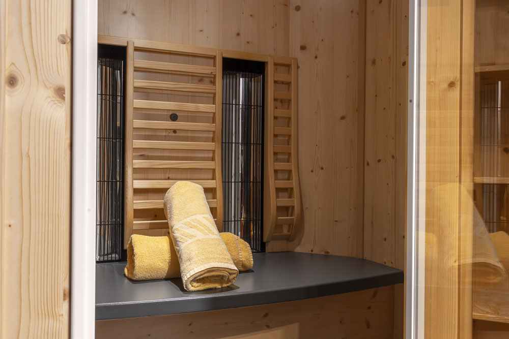 Der kleine Holzsaunaraum im Apartment Abendsonne im Alpenapart in Ladis verfügt über eine schwarze Bank und einen Holzpaneelofen. Drei gelbe Handtücher liegen ordentlich gefaltet auf der Bank, während helle Holzwände eine warme und einladende Atmosphäre schaffen.