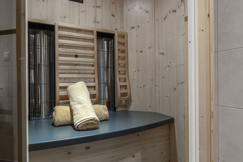 Im gemütlichen Apartment für 4 Personen im Alpenapart in Ladis erwartet Sie ein kleiner Saunaraum mit holzgetäfelten Wänden und einer Sitzbank. Drei gerollte Handtücher in Beige- und Gelbtönen liegen ordentlich auf der Sitzbank. Der Raum ist sanft beleuchtet und schafft eine warme und einladende Atmosphäre.