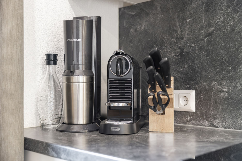 Soda-Maschine, Espresso-Maschine, Wasserflasche und Messerblock auf einer Küchenarbeitsplatte.