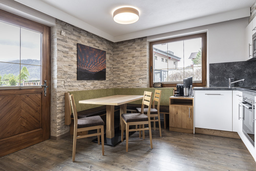 Gemütliche Küche mit Holzmöbeln, Steinwänden und großen Fenstern, die natürliches Licht hereinlassen.