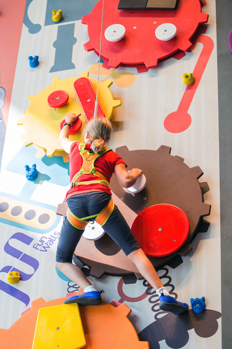 Ein Kind klettert in Serfaus-Fiss-Ladis an einer farbenfrohen Wand mit Zahnrädern, die sich perfekt für den Sommerurlaub eignet.