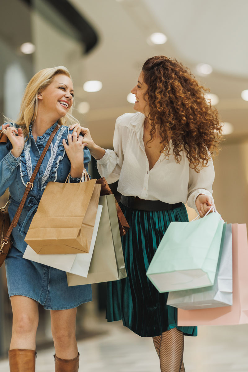 Zwei Frauen lächeln und tragen Einkaufstaschen in einem Einkaufszentrum.