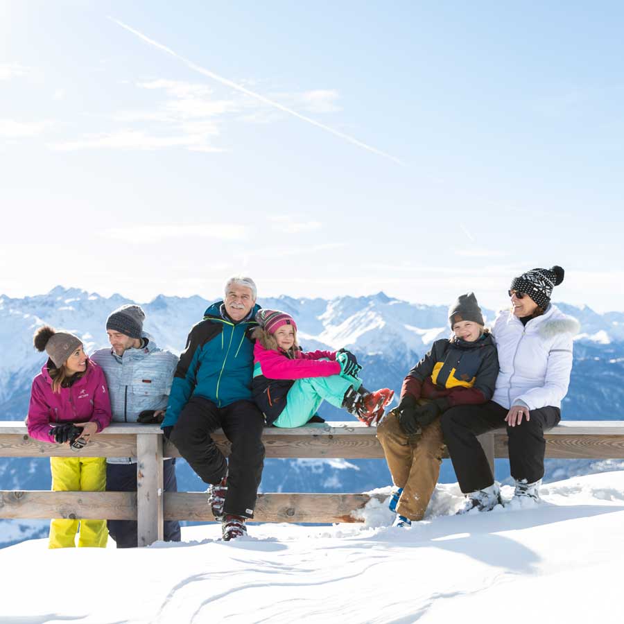 Sechs Personen in Winterkleidung sitzen auf einem verschneiten Zaun-7 Nächte bleiben 6 bezahlen.