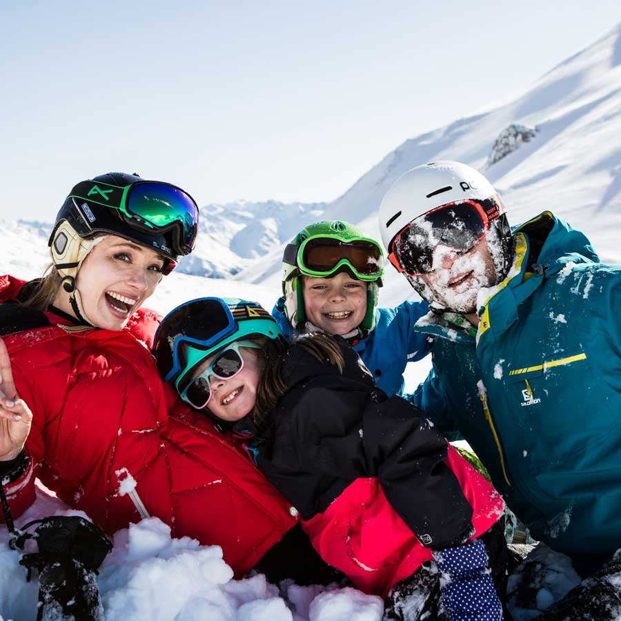 Vier Personen in Skikleidung, die lächelnd zusammen in den verschneiten Bergen posieren.